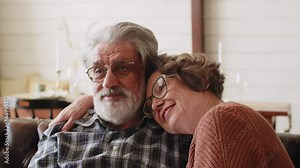 Happy older mature classy couple hugging, bonding, thinking of good future. Carefree mid age couple looking away dreaming together, enjoying comfort and wellbeing, feeling hope and pleasure at home.