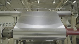 Paper sheet rolled by metal cylinders in production plant workshop closeup. Automatic equipment works at papermaking factory. Manufacture process