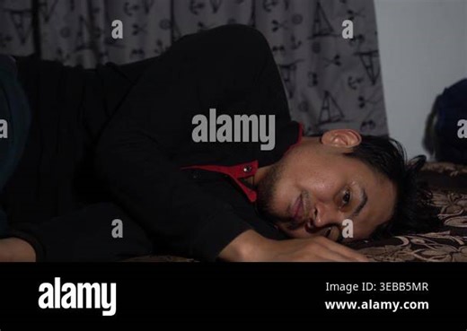 A thoughtful Southeast Asian man lying awake in bed at night, staring blankly with a sad expression. Themes of insomnia, depression, mental health struggle, loneliness, and contemplation in a dark bedroom setting. High-quality 4K cinematic footage Stock Video Footage - Alamy