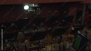 Empty orchestra pit before performance in classical theatre. Comfortable chairs and wooden music stands with lighting fixtures stand side by side. Workplace of orchestra during intermission.
