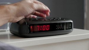 Alarm clock digital ringing, 7am, tired man pushes if of bed table