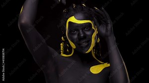 Face art. Dancing woman with black and yellow body paint. Young african girl with colorful bodypaint. An amazing afro american model with yellow makeup. Closeup face.