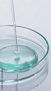 Dripping liquid from pipette into petri dish at white table, closeup