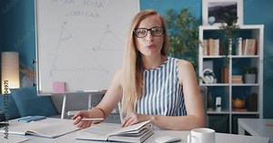 Attractive woman explaining math material for students through video call, point of view. Competent teacher using computer at home office.
