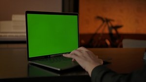 Faceless male typing something on green screen laptop keyboard. Only fingers and hands, cozy home evening light interior. Place for pasting content on chromakey display.
