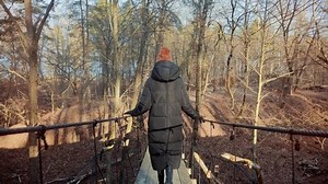 Woman Walking On Suspension Bridge. Tourist Walkway In Forest. Traveler Explore Forest. Wanderlust Travel Searching Right Direction. Legs Walking On Suspension Wooden Bridge. Rope Bridge In Fall Park