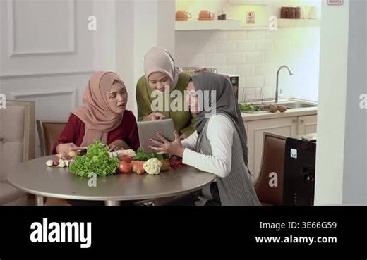Three asian women cooking together in modern kitchen wearing hijab, sharing tablet recipe, chopping vegetables and arranging Stock Video Footage - Alamy