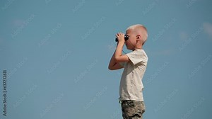 A young boy explorer looks through binoculars. A child traveler learns to navigate the terrain. An active boy on a journey looks through binoculars. Tourism education. School of Tourism and Travel