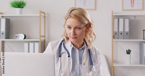 Female doctor or nurse working remotely with a laptop, taking notes in a hospital office. Utilizing the internet for online work, she demonstrates the flexibility and efficiency medical practices.