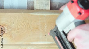 Video of carpenter male hands working with pneumatic stapler for wooden timber board. Clipping and scoring metal nails and staples, making layout on wooden plank. Nailer technology for wood framework