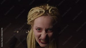 Close-up portrait of eerie attractive woman vampire hungry for fresh blood, frightening and moving aggressively in darkness, showing her bloody pale face, expressing horror and danger on halloween.