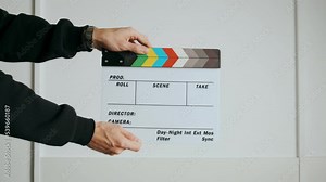 A punch on a cinematic slate or clapper board. Close-up of a hand holding an empty slate board and slapping it against a white background. White studio background. Opening and closing slate board for