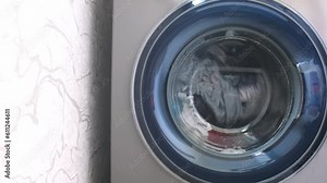 The washing machine washes dirty colored clothes. Washing clothes in a household washing machine. Close-up of the rotation of a drum washing machine.