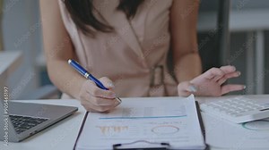 Female accountant analyzing financial documents and using a calculator in an office setting. Showcase financial work with a laptop and data charts
