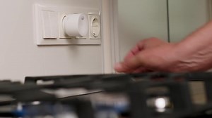 Hand Installing a Compact Gas Detector into Wall Socket Near Kitchen Stove for Safety Monitoring