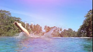 SLOW MOTION, CLOSE UP, LENS FLARE: Young woman in pink bikini jumping head first into infinity pool in luxury resort in lush palm tree jungle on sunny tropical island. Girl enjoying summer vacation