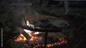 Outdoor nighttime barbecue with a beef cut slow-cooking over a fire - slow motion