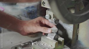 Camera moving towards hands of anonymous artisan putting piece of mosaic material on sharp machine and cutting it on halves