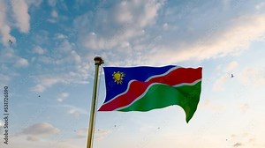 Flag of Namibia waving in the wind, sky and sun background. Namibia Flag. 4K Ultra Hd.