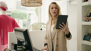 Young blonde woman shop assistant using touchpad working at clothing store