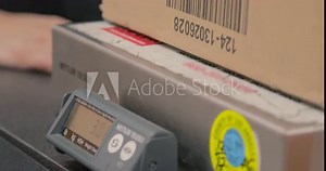 Weighing a package on a scale. Postal worker sets a box on a scale to get weight in poinds. Shot in 4k 30fps slow motion.