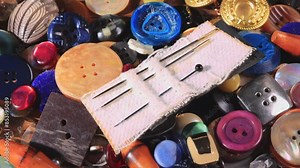 Sewing needles on colorful dress buttons. Old clothe buttons collection. Different types of decorative buttons for use on bags, clothes, wallets. Slow pan to the right. Close up, moving slider shot