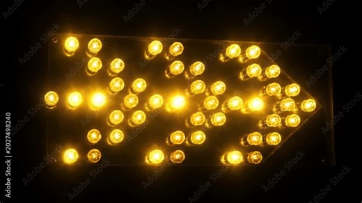 Bright Yellow Arrow Sign Illuminated with Numerous Lights at Night.