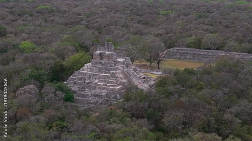 A sweeping aerial drone flyover of the ancient Mayan city of Edzná in Campeche, Mexico. The footage reveals the full layout of the archaeological site, including pyramids, plazas, and the jungle