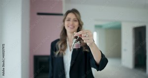 Blonde real estate agent delicately holds contract plan gracefully extends the keys towards the camera, symbolizing the seamless transition from house hunting to the blissful reality of homeownership.