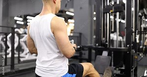 Male bodybuilder doing exercises for muscles of back and arms on sports simulator 4k movie slow motion. Sport and beautiful figure concept
