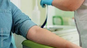 Professional female lab assistant in gloves applying tourniquet on male patient arm before taking venous blood for test, intravenous injection. Experienced doctor preparing for blood sample collection