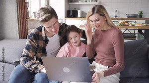 Happy family young parents and kid child daughter using laptop computer technology device having fun sitting on couch at home, talking, laughing doing ecommerce shopping online, e learning together.