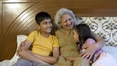 Happy indian grandmother with grandparents talking in bed. Grandma...