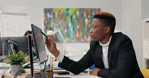 Handsome dark-skinned man, corporate office worker spends morning in front of computer, points at screen, counts, ponders, checks correctness of graphs, completes data