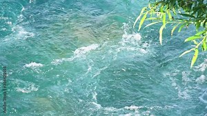 Closeup of rushing water flow in Waimakariri River, slow motion, green foliage in the foreground, New Zealand