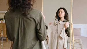 Young woman getting dressed looking in mirror. Trying on clothes enjoying herself.