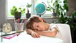 Little schoolboy boy fell asleep at a table doing homework lessons, fatigue first-grader