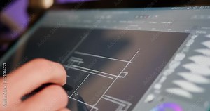 An architect sketching and drafting out blueprints or concept art for a building project on a digital graphic tablet in a design studio.