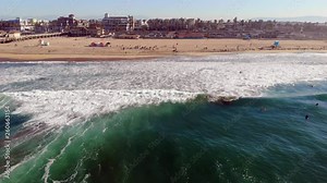 Wide aerial 4k drone boom down of Huntington Beach shore from over ocean waves, looking back at downtown and beach sand with surf in foreground at sunrise, Pacific Ocean, Southern California