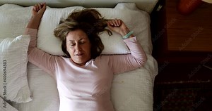 Older woman lying down in bed taking a rest. Senior person napping, falling asleep