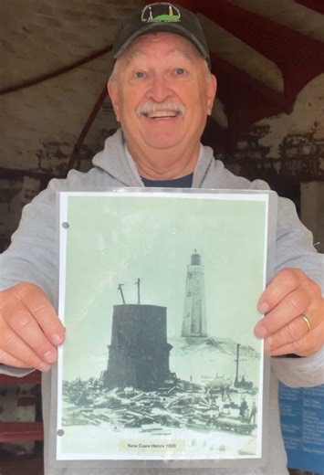📸 who’s behind the camera?? #capehenrylighthouse #virginiabeach #history #mystery #photography VD: A man with a white mustache wearing a dark ballcap and a light gray sweatshirt stands inside the Old Cape Henry Lighthouse holding a reproduction of a c.1880 black and white photograph of the New Cape Henry Lighthouse under construction in the foreground with the Old Cape Henry Lighthouse in the background.