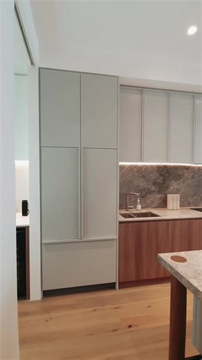 This thoughtfully designed modern residence showcases a seamless integration of style and functionality. The living area features custom cabinetry, ambient lighting, and rich textures that create a warm yet sophisticated atmosphere. Adjacent, the minimalist kitchen pairs natural stone surfaces with sleek wood finishes and integrated lighting, offering both elegance and efficiency in one harmonious space. #ModernHome #InteriorDesign #LuxuryLiving #HomeInspo #MinimalistDesign #CustomCabinetry #Amb