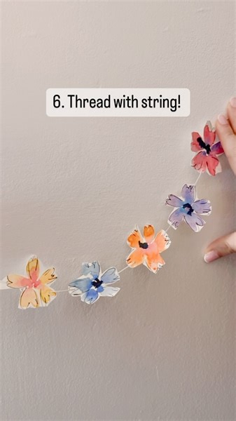 How to: Watercolour Flower Garland 1. For the petals, paint two brush strokes by flattening the belly of the brush on the paper and dragging upwards. Repeat this until you have a full flower. Make sure you leave a gap in the centre of the flower. 2. When the flower is almost dry, tap a different colour at the centre of the petals. 3. Fill a sheet of paper with the flowers. 4. Once they’re dry, use a black ink pen to draw around the petals. 5. Cut the flowers out. 6. Thread them in to string. And