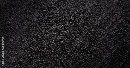 Macro Black Rough Texture Background. A seamless, slow panning footage across a deep black grainy surface revealing tactile depth through gentle shadow shifts and minimal highlights.
