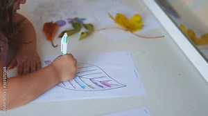 Little girl coloring a big leaf image on a paper sheet with a pen