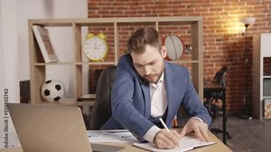 A young man in the office speaks on the phone and writes something in a notebook, then looks at the laptop and begins to actively gesticulate. Slow motion 4k footage