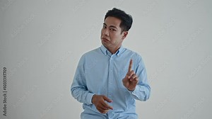 Medium shot of young Asian man in blue shirt shrugging while doubting, refusing or saying no problem, and forbidding on camera on white background