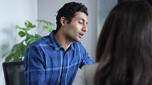 Young Indian man job seeker sit at desk in female hr office speak about herself describe experience. Confident Asian male candidate on vacant place answer recruiter question based on resume.