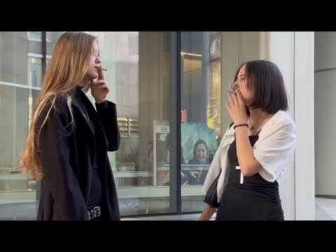 Two beautiful girls in short dresses smoke a cigarette, throw it on the floor and spit.