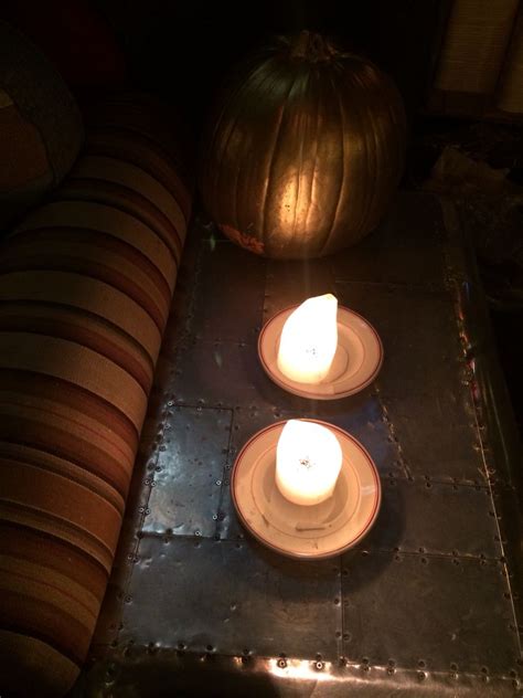 Two Lit Candles Sit On Plates Next To A Pumpkin